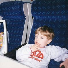 a young boy sitting in an airplane seat eating something out of his hand and looking at the camera