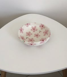 a bowl sitting on top of a white table next to a wooden leg vase with pink flowers