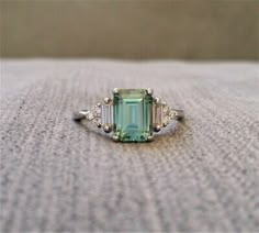 an emerald and diamond ring sitting on top of a carpeted floor in front of a wall