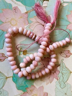 three pink beads with tassels are on a floral tablecloth and one is in the shape of a heart