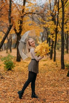 a woman is holding an umbrella in the woods with autumn leaves on the ground around her