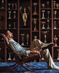 a man sitting on a chair in front of a book shelf filled with trophy trophies