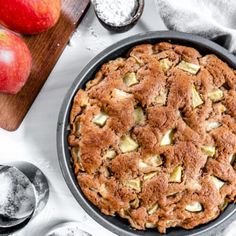 an apple pie sitting on top of a pan next to two apples and spoons