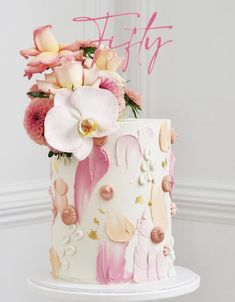 a pink and white cake with flowers on top that says pretty written in large letters