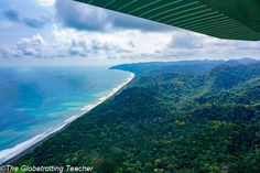 the view from inside an airplane looking out over trees and mountains to the ocean below