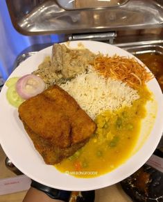 a white plate topped with meat and rice covered in gravy next to other foods