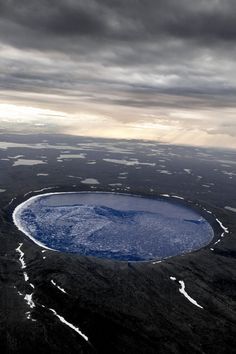 an aerial view of a blue lake surrounded by mountains under a dark sky with clouds