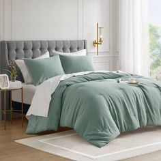 a bed with green comforter and pillows in a room next to a white rug