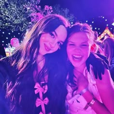 two girls are posing for the camera in front of some people at an event with bright lights