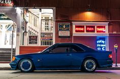 a blue car is parked in front of a building with neon signs on the windows