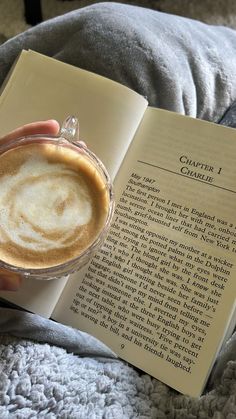 a person is reading a book and holding a cup of cappuccino in their hand