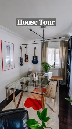 a living room with a glass table and guitars on the wall above it, in front of a black leather couch