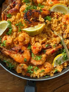 a pan filled with shrimp and rice topped with lemon wedges