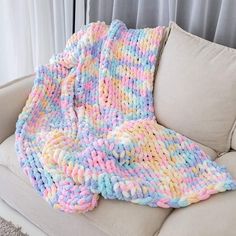 a multicolored knitted blanket sitting on top of a couch next to a window