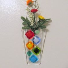 there is a vase with flowers in it that has different colored glass cubes on the bottom