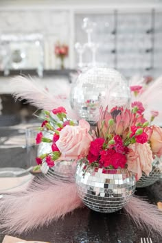 a disco ball centerpiece with pink flowers and feathers on a dining room table set for a party