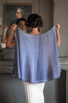 a woman is looking at herself in the mirror while holding up a blue shawl