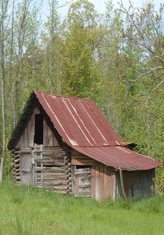 an old log cabin sits in the middle of a field with tall grass and trees