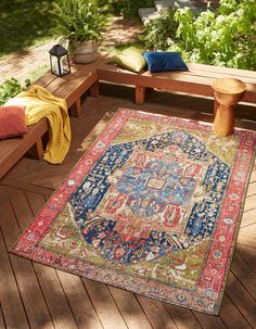 a colorful rug on a wooden deck with benches and potted plants in the background