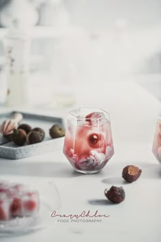 two glasses filled with liquid sitting on top of a table next to nuts and fruit