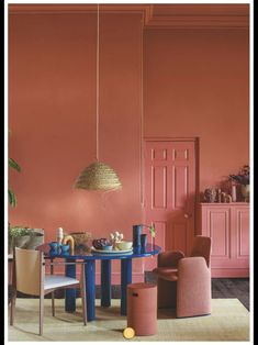 a dining room with pink walls and blue table in the center, chairs around it