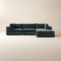 a large sectional couch with pillows on the top and bottom, sitting in front of a beige wall