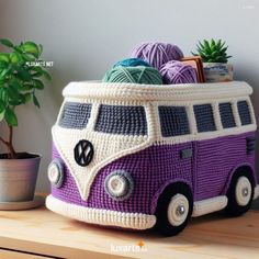 a crocheted purple and white bus with yarn on it next to a potted plant