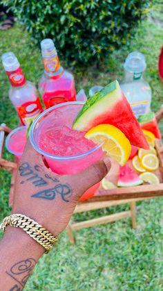 a person holding up a drink in front of some watermelon and lemons