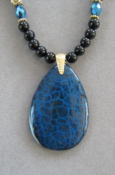 NOTE: Fire Agates are natural volcanic stone and they are not perfect due to the nature of the stone. However, they are very pretty! The pendant is unusual and it is thicker than most because it comes from volcanic rock. This is a lovely teardrop shaped Black and Blue Fire Agate Pendant Necklace.   The beads in the necklace are genuine black agate with blue crystal beads that pick up the colors of the pendant with silver crystal accents.   The pendant is polished. The pendant measures 2 inches long x 1 1/2 inches wide.  This is a unique one of a kind necklace.  It's 16 inches long and adjustable to 20.  All my jewelry is unique and one of a kind. Similar quality jewelry is priced at double. I source the stone pendants from all over the world. All pendants and necklaces are made with semipr Jean Art, Blue Crystal Beads, Agate Pendant Necklace, Volcanic Stone, Volcanic Rock, Fire Agate, Blue Fire, Black Agate, Silver Crystal