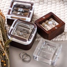 three personalized wedding rings in wooden boxes on a table with pine needles and dried flowers