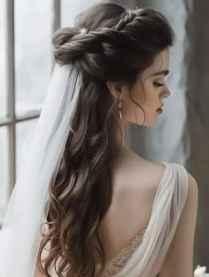 a woman with long hair wearing a wedding dress and veil is looking out the window