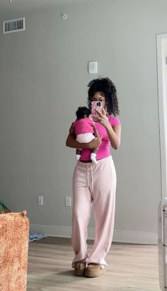 a woman holding a baby taking a selfie in the mirror while wearing pink clothing