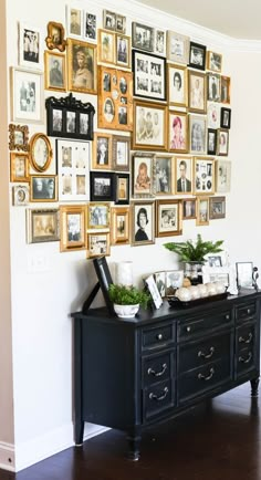 a black dresser sitting in front of a wall filled with pictures and framed photos on it