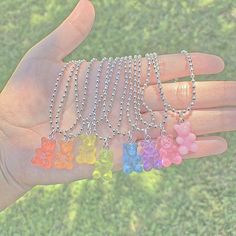 a person's hand holding several different colored teddy bears on chain necklaces in the grass