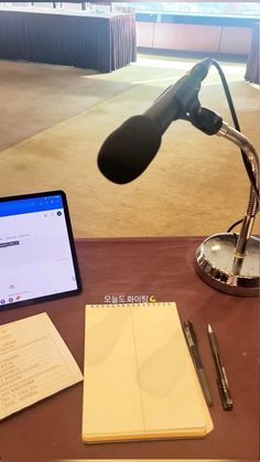 a desk with a laptop, pen and microphone on it next to a notepad