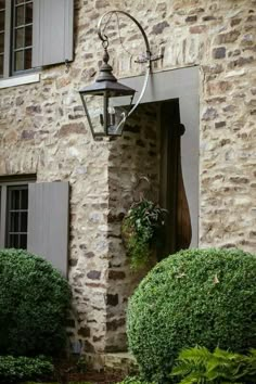 an old fashioned light hanging from the side of a stone building next to some bushes