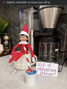 an elf is sitting in a coffee cup next to a sign that says, nightly reminder to move your elf