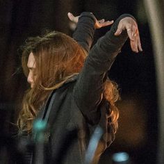 a woman with red hair is holding her hand out in the air while standing outside