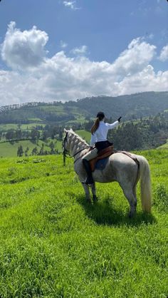 a woman riding on the back of a white horse in a lush green field under a blue sky