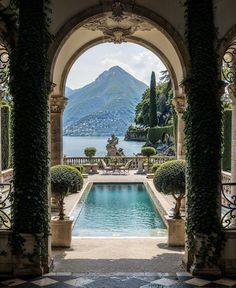 an outdoor swimming pool surrounded by greenery and stone arches with mountains in the background