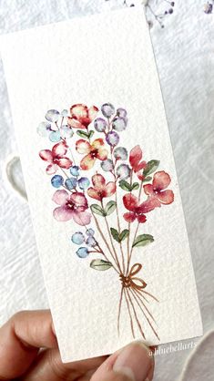 a person holding up a card with watercolor flowers on it