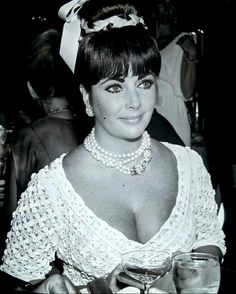 a woman in a white dress holding a glass and posing for the camera with other people behind her