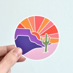 a person holding up a sticker with a cactus in the middle and sunset behind it