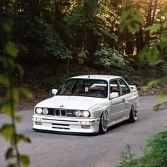 a white car driving down a road next to some trees in the sun shining on it's headlight