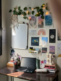 a laptop computer sitting on top of a wooden desk next to a wall covered in pictures