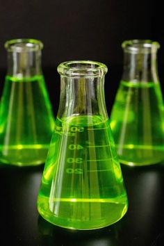 three green flasks filled with liquid on a table next to a black background