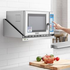 a person is holding up a microwave over a cutting board with tomatoes and peppers on it