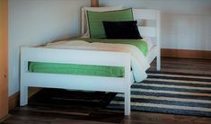 a white bed with green pillows on top of it and a rug in front of it