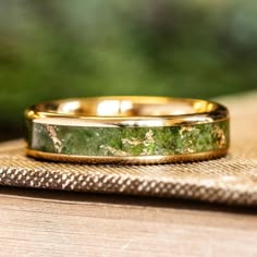 a close up of a wedding ring on top of a piece of wood with trees in the background