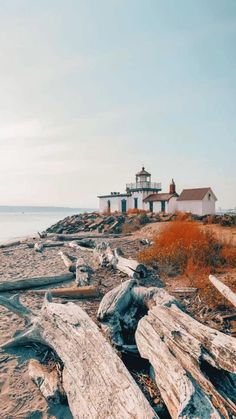 an old log laying on the beach next to some water and a light house in the background